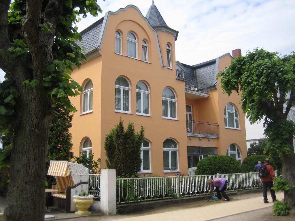 a large yellow house with people standing in front of it at Hotel Villa Strandrose in Ahlbeck