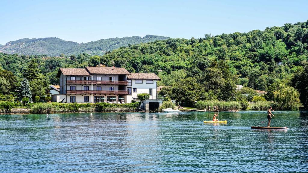 two people on paddle boards in the water in front of a house at Cascina Tumas Orta Lake in Pettenasco