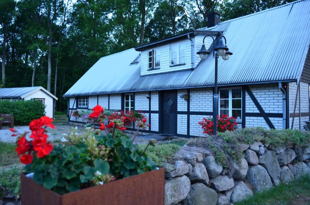 uma casa branca com um telhado de metal e flores vermelhas em Smedsgården em Höganäs