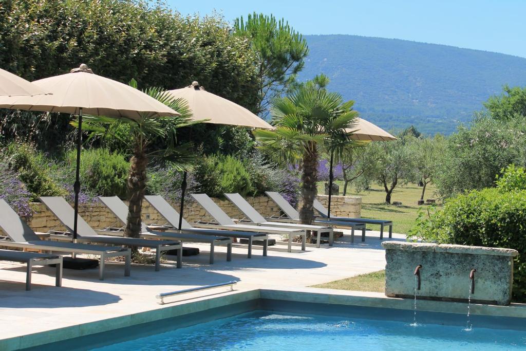 a group of chairs and umbrellas next to a pool at Le Mas Les Eydins in Bonnieux