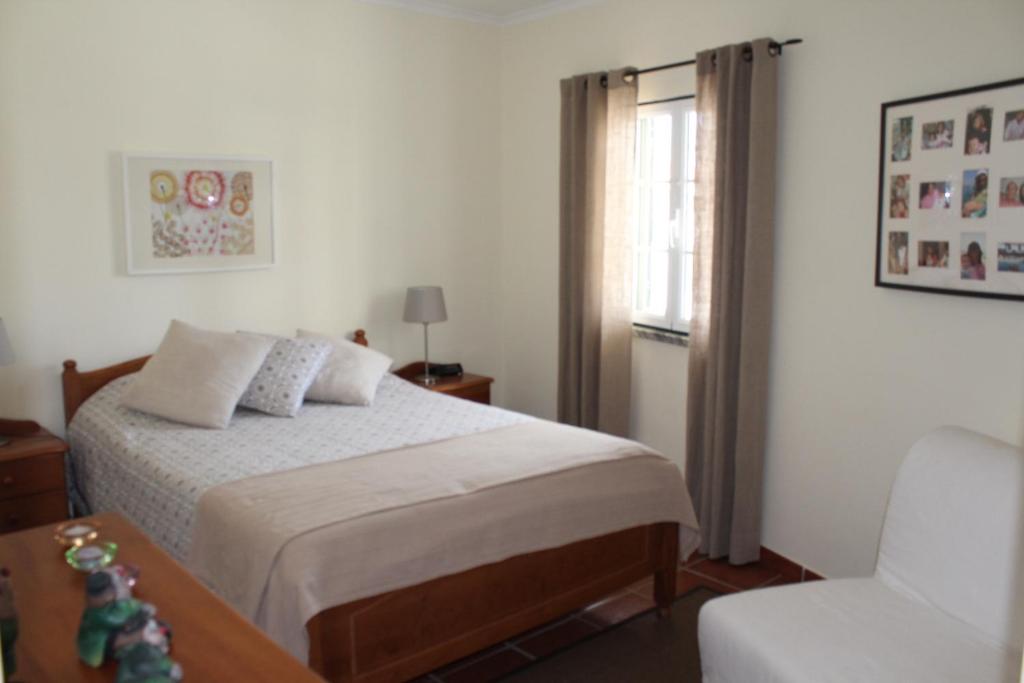 a bedroom with a bed and a chair and a window at Apartamento de São João in Praia da Areia Branca