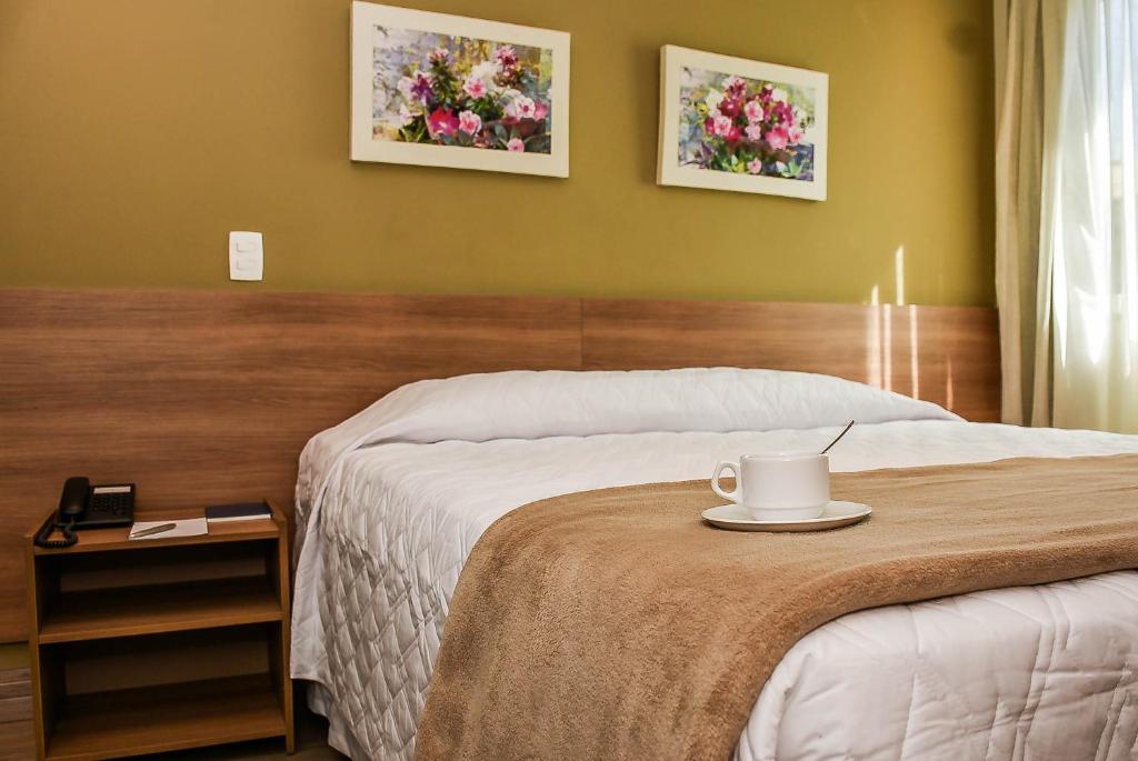 a hotel room with a bed with a cup on a table at Mont Blanc Suites Duque de Caxias in Duque de Caxias