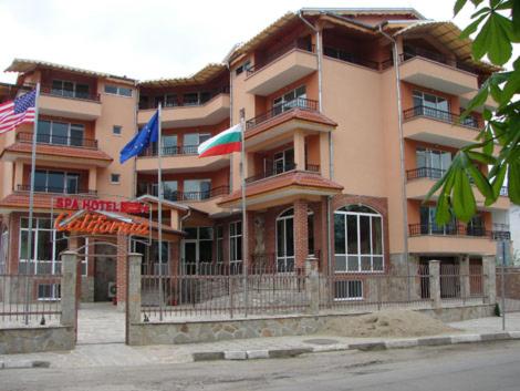 een groot gebouw met vlaggen ervoor bij Спа Хотел Калифорния in Pavel Banya
