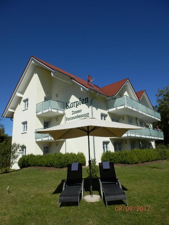 a building with two chairs and an umbrella in the grass at Hotel & Restaurant Karpfen in Illmensee