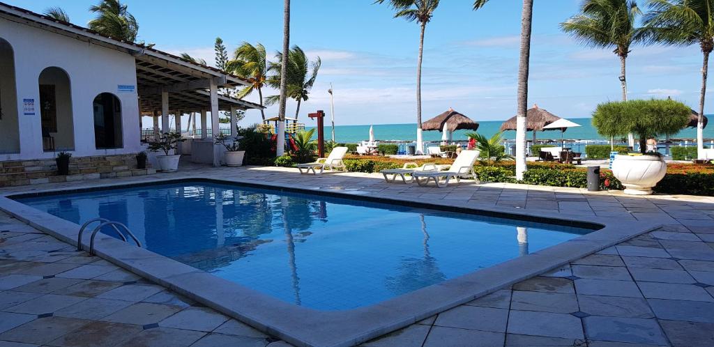 uma piscina com palmeiras e o oceano em APART HOTEL MARINAS TAMANDARÉ - Flat 104 em Tamandaré