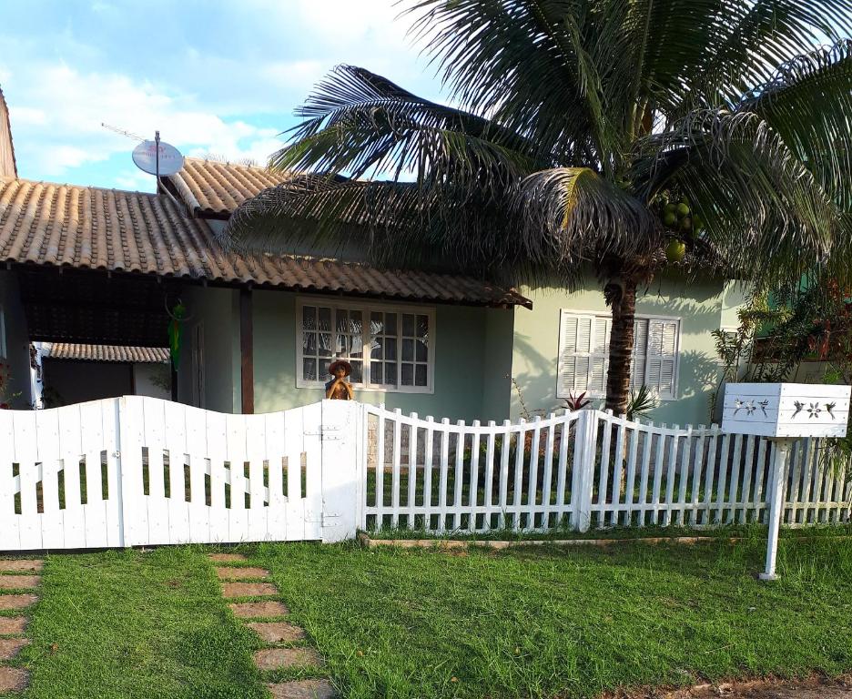 una cerca blanca frente a una casa con una palmera en Casa em Unamar,Cabo Frio,à 200m da praia,em condomínio com segurança 24 hs, en Cabo Frío