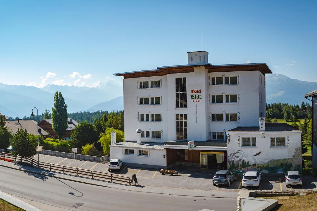 um grande edifício branco com carros estacionados num parque de estacionamento em Hotel Elite em Crans-Montana