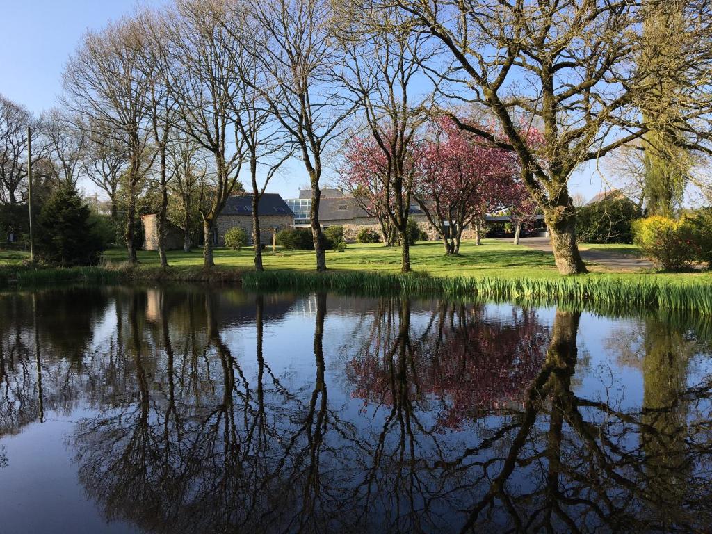 a pond with trees and a building in the background at Kericouette et Délices in Le Vieux-Bourg