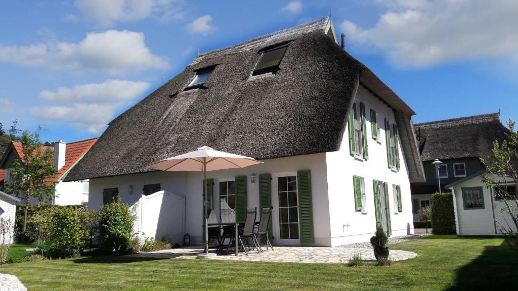 une maison blanche avec un toit noir et un parasol dans l'établissement Ahornweg 7a, à Karlshagen