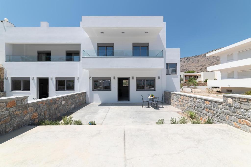 a large white house with a stone wall at Aegean Treasure Pefkos in Pefki
