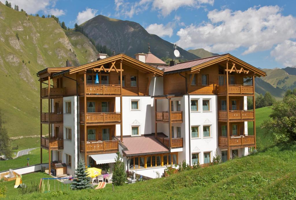 a building on a hill with mountains in the background at Apart-Garni Motnaida in Samnaun