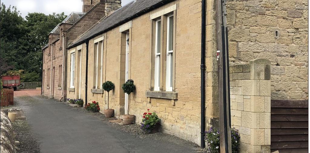 uma fila de casas de tijolos com vasos de plantas em Purves Cottage em Allanton