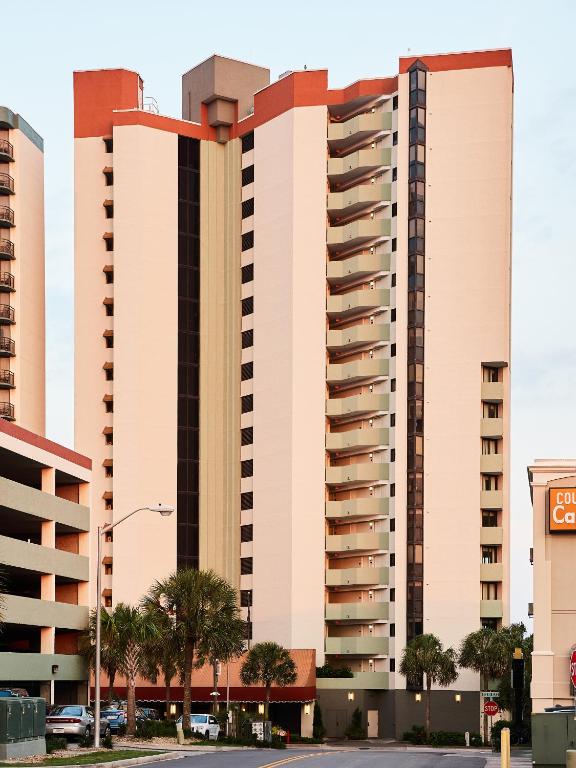 a large building with palm trees in front of a street at The Strand - A Boutique Resort in Myrtle Beach