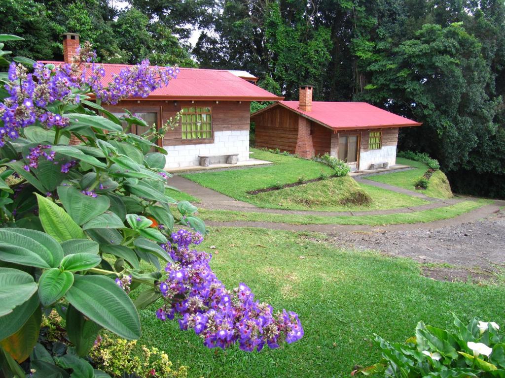 Rancho Amalia في Naranjo: منزل به سقف احمر وبعض الزهور الارجوانية