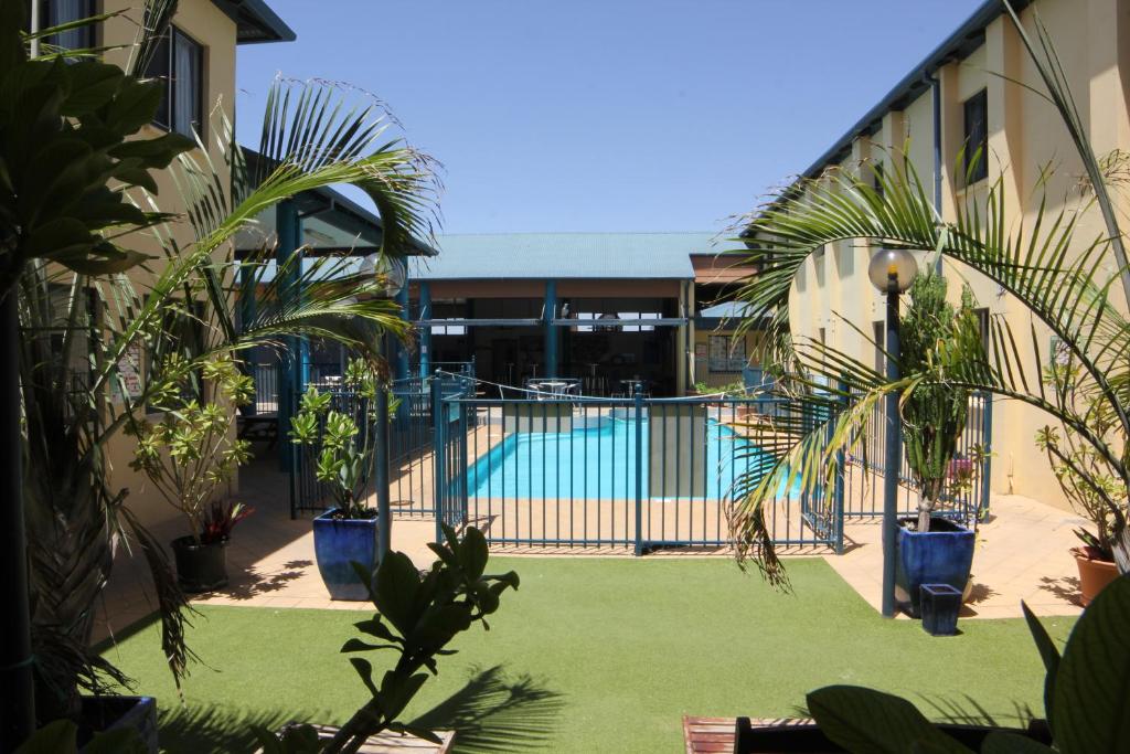 une cour avec une piscine bordée de palmiers et une clôture dans l'établissement Ningaloo Club Backpackers, à Coral Bay