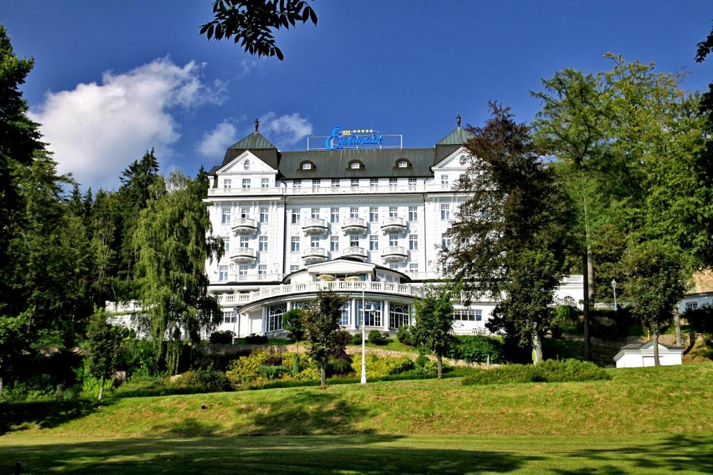 a large white building on a hill with trees at Esplanade Spa and Golf Resort in Mariánské Lázně