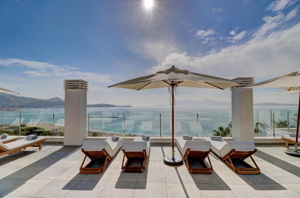 d'une terrasse avec des tables, des chaises et un parasol. dans l'établissement Hoposa Pollentia - Adults Only, à Port de Pollença