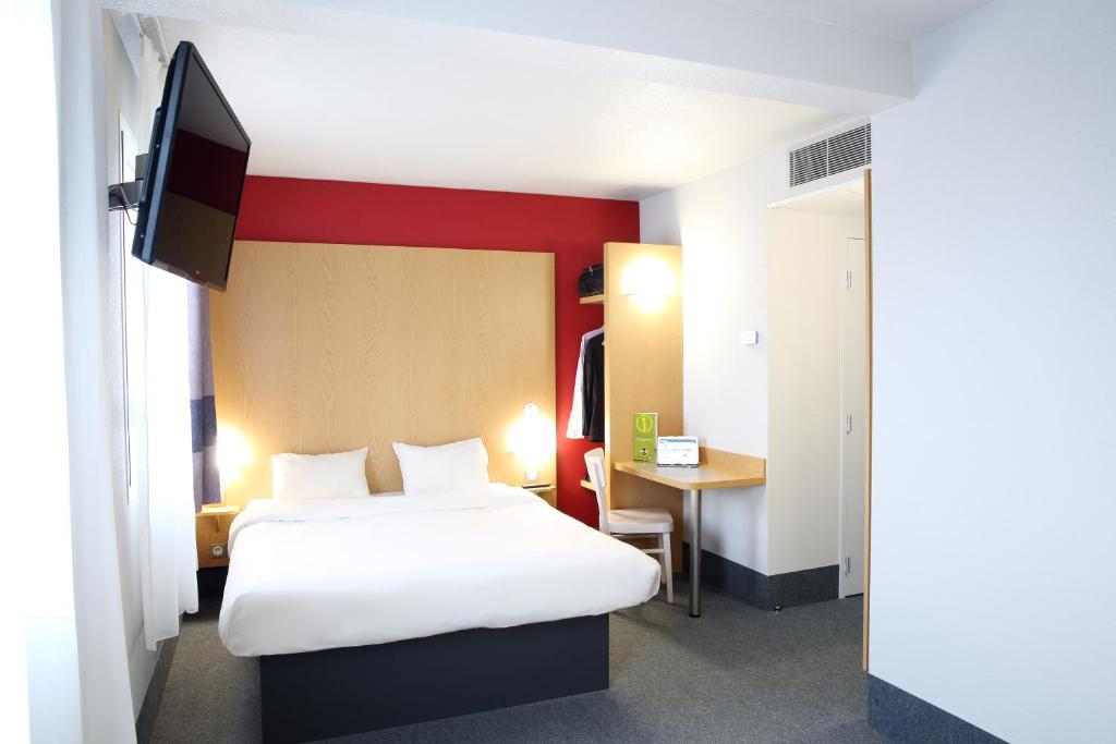 a room with two beds and a desk and a tv at B&B HOTEL Perpignan Sud Marché International in Perpignan