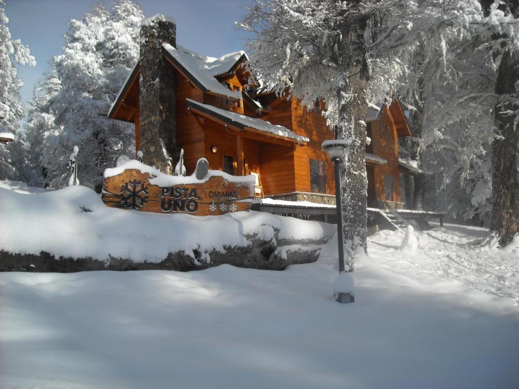 uma cabana de madeira na neve com uma placa à frente em Cabañas Pista Uno Ski Village em San Martín de los Andes