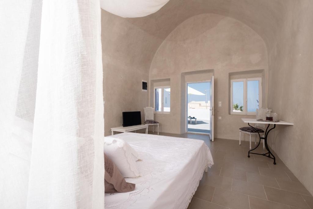 a bedroom with a white bed and a desk and windows at DeltaMi Santorini in Pirgos