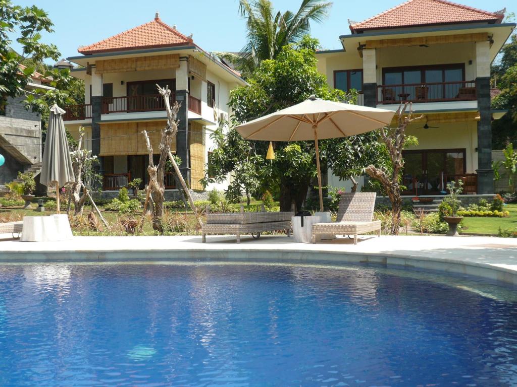 een zwembad met twee stoelen en een parasol en een huis bij Sukun Babonsay Villas in Amed