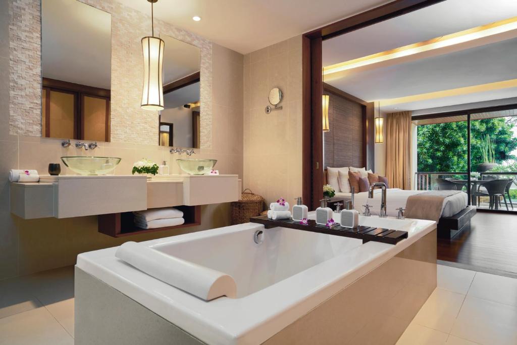 a bathroom with a large tub and a bedroom at Mövenpick Resort Bangtao Beach Phuket in Bang Tao Beach