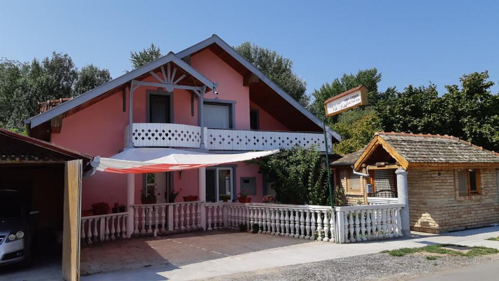 ein rosafarbenes Haus mit einem weißen Zaun und einem Gebäude in der Unterkunft Villa Anna in Palić