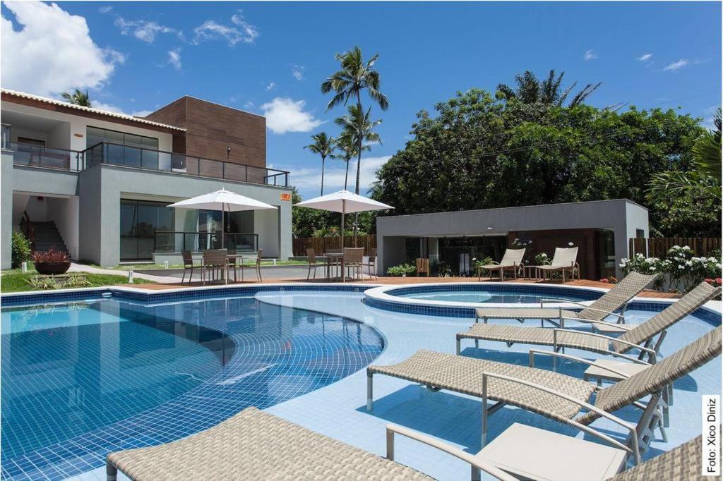 a swimming pool with chairs and a house at Condominio Solaris Imbassaí in Imbassai