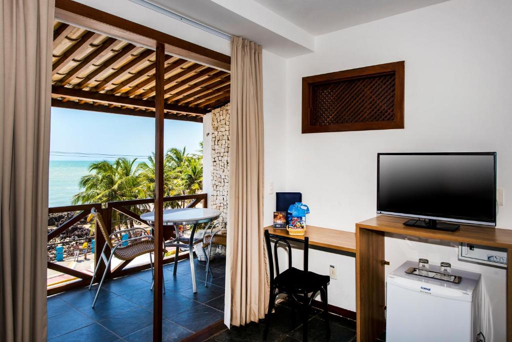 um quarto com uma televisão e uma varanda com o oceano em La Belle Beach Hotel em Natal