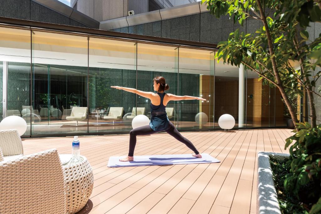 a woman doing a yoga pose on a yoga mat in a courtyard at Cerulean Tower Tokyu Hotel, A Pan Pacific Partner Hotel in Tokyo