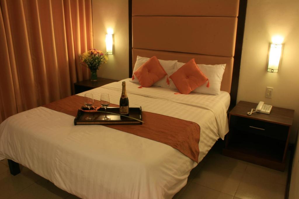 a hotel room with a bed with a tray with a bottle and glasses at O Hotel in Bacolod