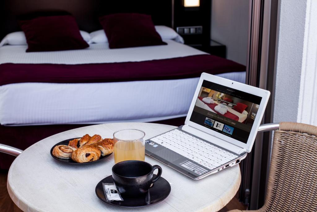 einen Tisch mit einem Laptop und einer Tasse Kaffee und Croissants in der Unterkunft Clement Barajas in Madrid