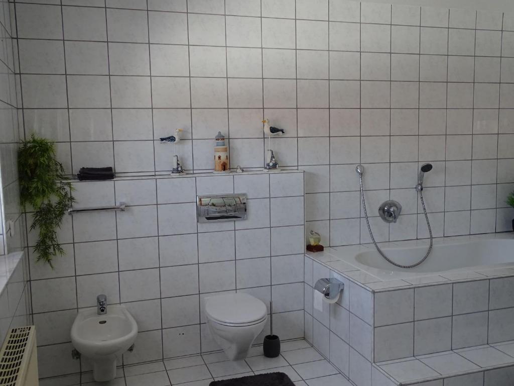 a white tiled bathroom with a toilet and a sink at Ferienhaus Fam. Bisgen in Niederkirchen bei Deidesheim