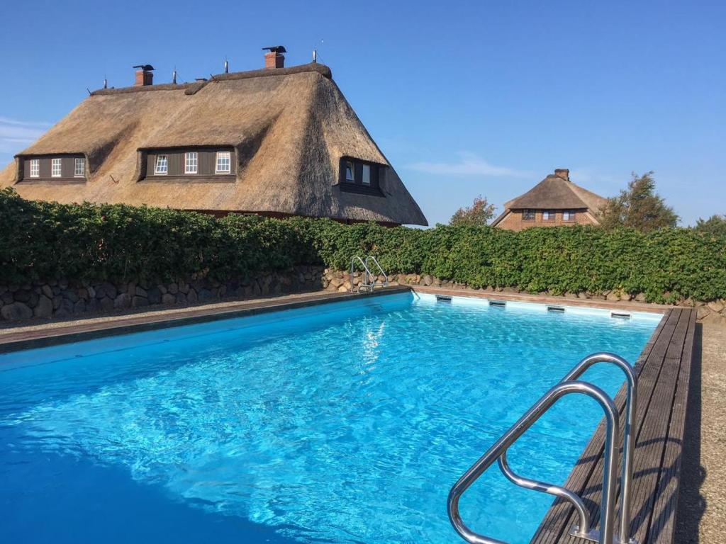 una piscina di fronte a una casa con tetto di paglia di Haus Wattblick Meier W.O. a Braderup