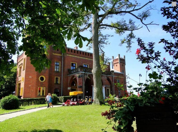 a large brick building with people walking in front of it at Hotel Zamek Karnity in Miłomłyn