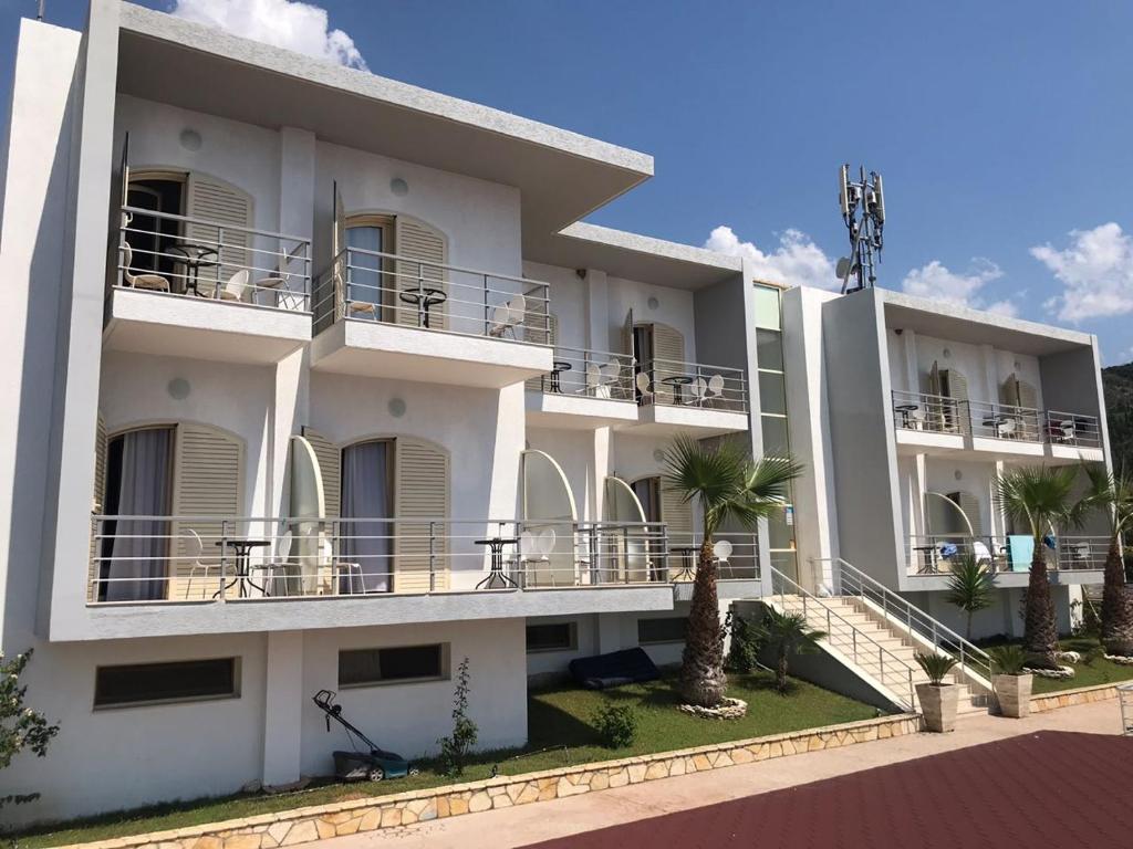 a white apartment building with balconies and palm trees at Royal Blue Hotel in Dhërmi