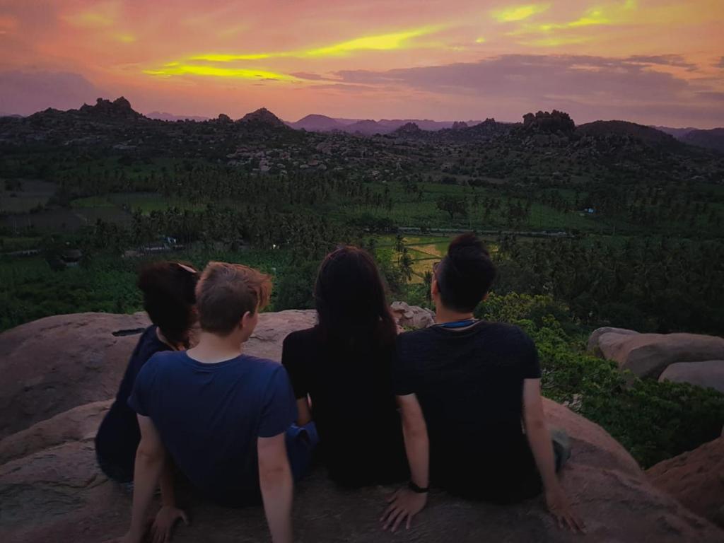 a group of people sitting on a rock watching the sunset at Thilak Home Stay in Hampi