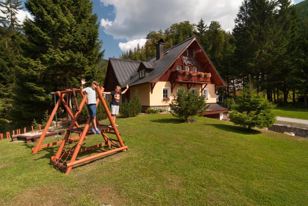 2 personnes debout sur une aire de jeux en face d'une maison dans l'établissement Pension Katty, à Špindlerův Mlýn