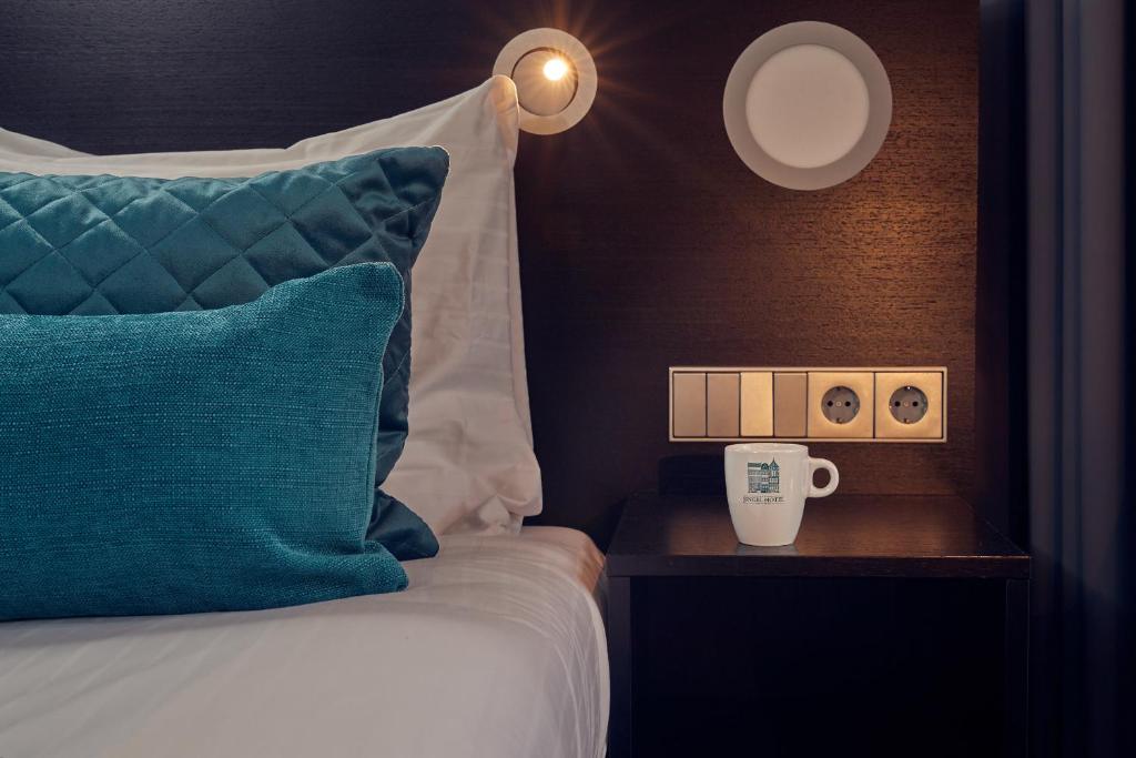a bed with a blue pillow and a cup on a night stand at Singel Hotel Amsterdam in Amsterdam