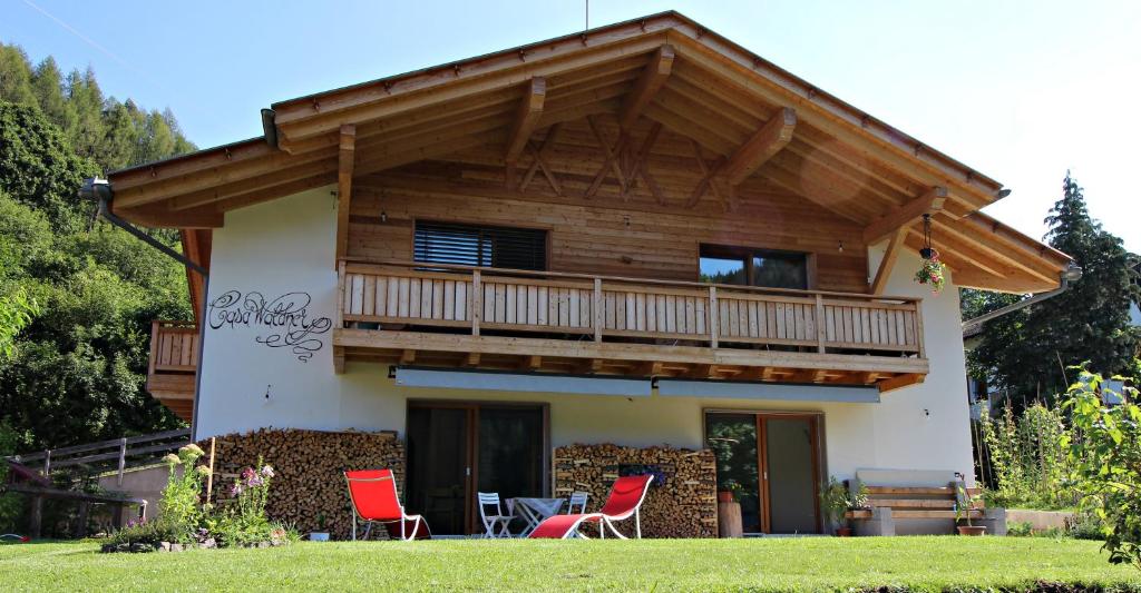 a house with a balcony and red chairs at casa waldner in Castello di Fiemme