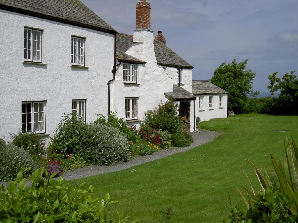 Crackington HavenにあるLower Tresmorn Farmhouseの草の庭のある古い白い家