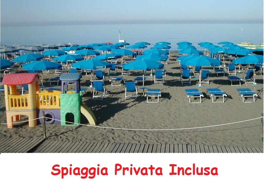 un mucchio di sedie e ombrelloni su una spiaggia di Hotel Flora a Marina di Bibbona