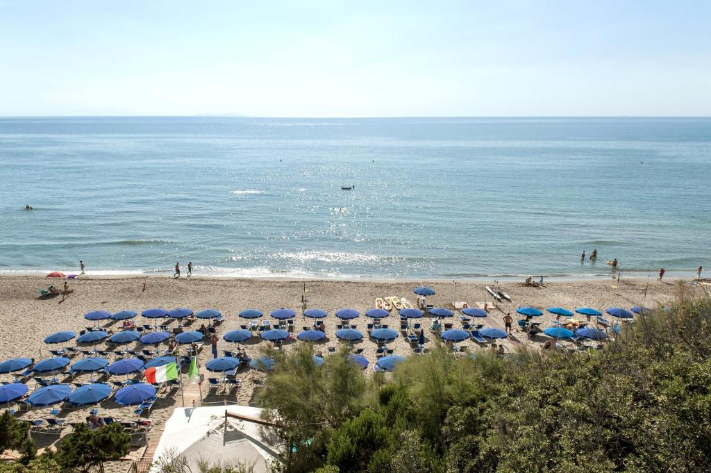 a beach with many blue umbrellas and the ocean at Hotel Villa Lo Scoglietto in San Vincenzo