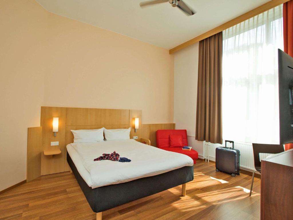 um quarto de hotel com uma cama e uma cadeira vermelha em ibis Berlin City Süd em Berlim