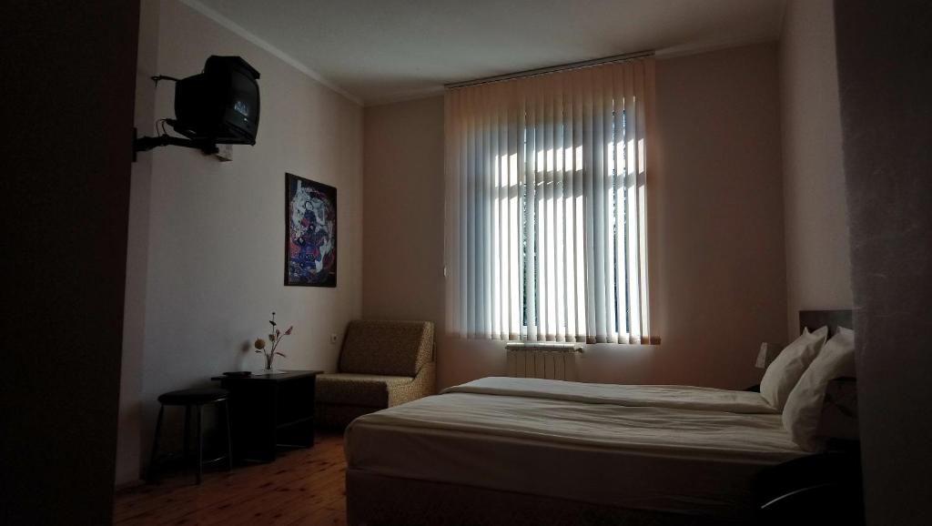 a bedroom with a bed and a window and a chair at семеен хотел "НЕВЕН" in Momin Prohod