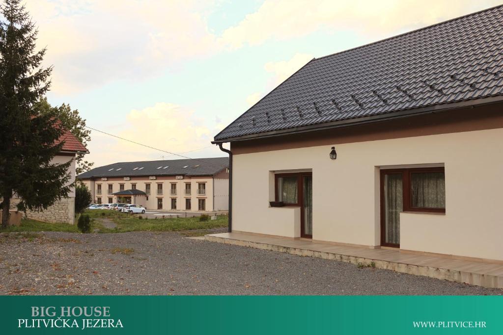 a white house with a building in the background at House Korina B&B in Ličko Petrovo Selo