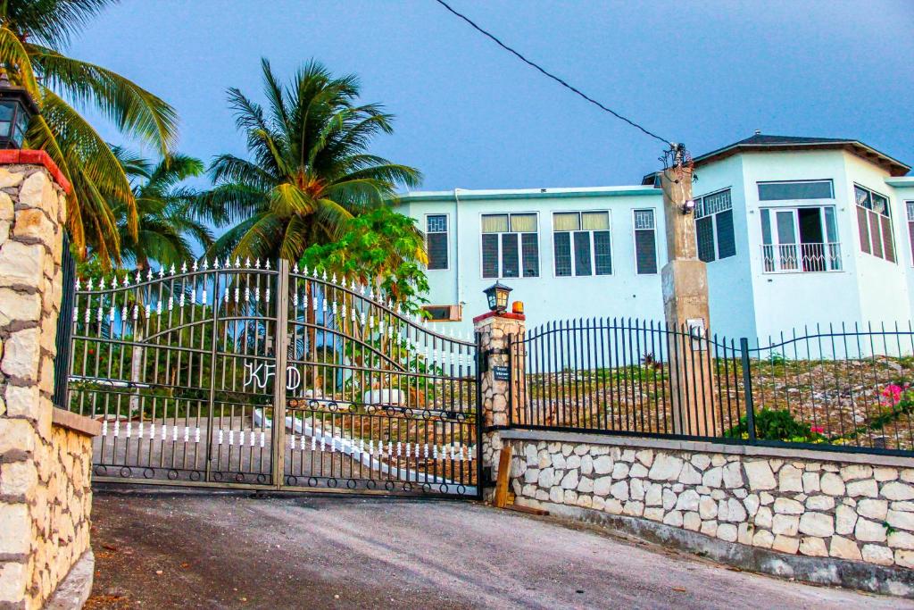 a fence in front of a white house with a palm tree at Sunshine Lodge: Your home away from home in Montego Bay