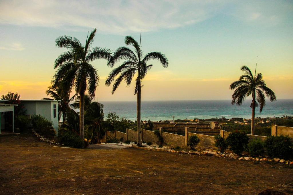 two palm trees in front of the ocean at sunset at Sunshine Lodge: Your home away from home in Montego Bay