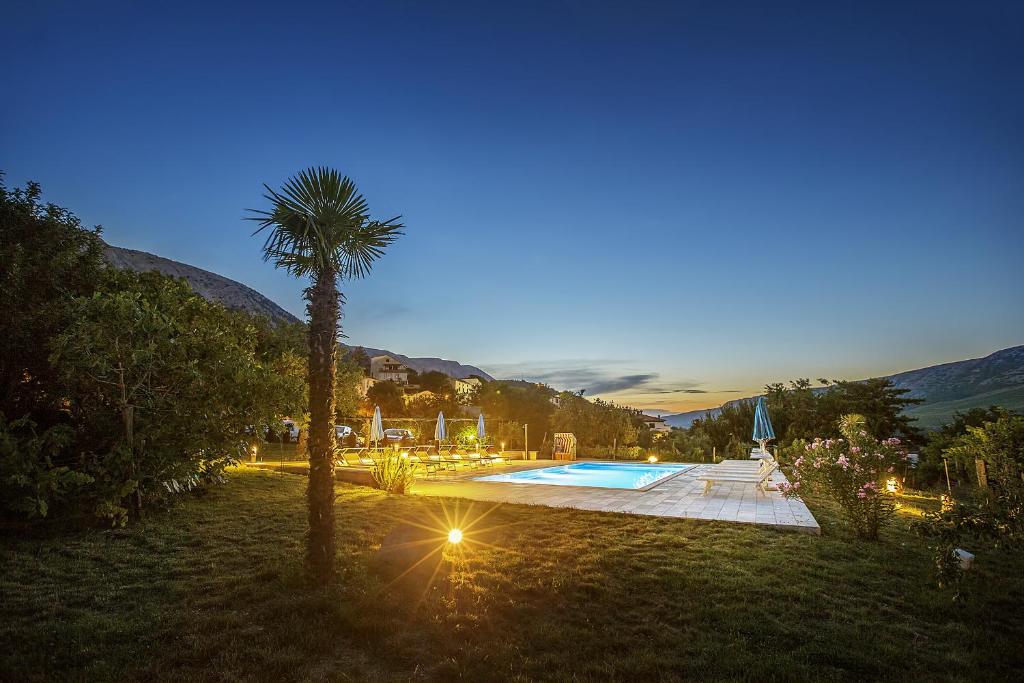 a palm tree next to a swimming pool at night at Apartments Juranic I in Baška