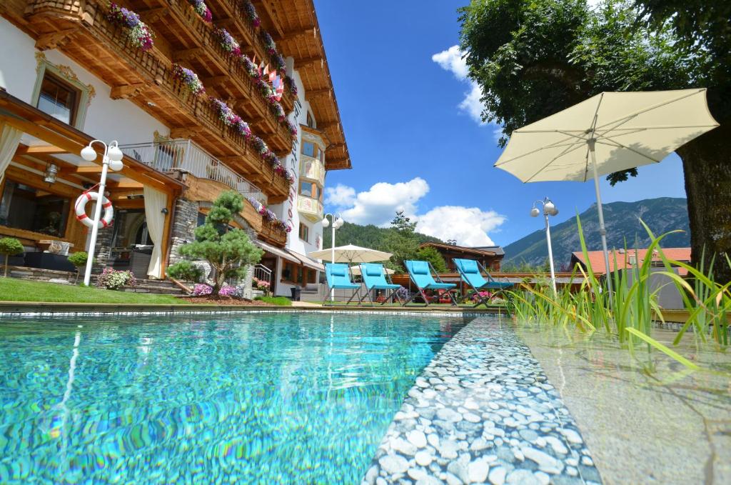 ein Pool mit Sonnenschirm neben einem Gebäude in der Unterkunft Alpenhotel Tyrol - Konzepthotel - adults only in Pertisau